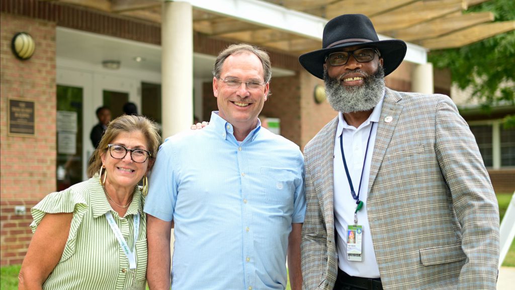 Three smiling people posing outdoors near building entrance