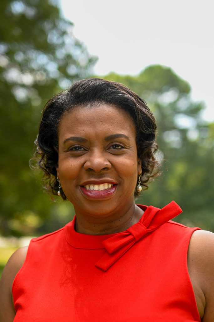 Smiling woman wearing red dress with bow detail and pearl earrings