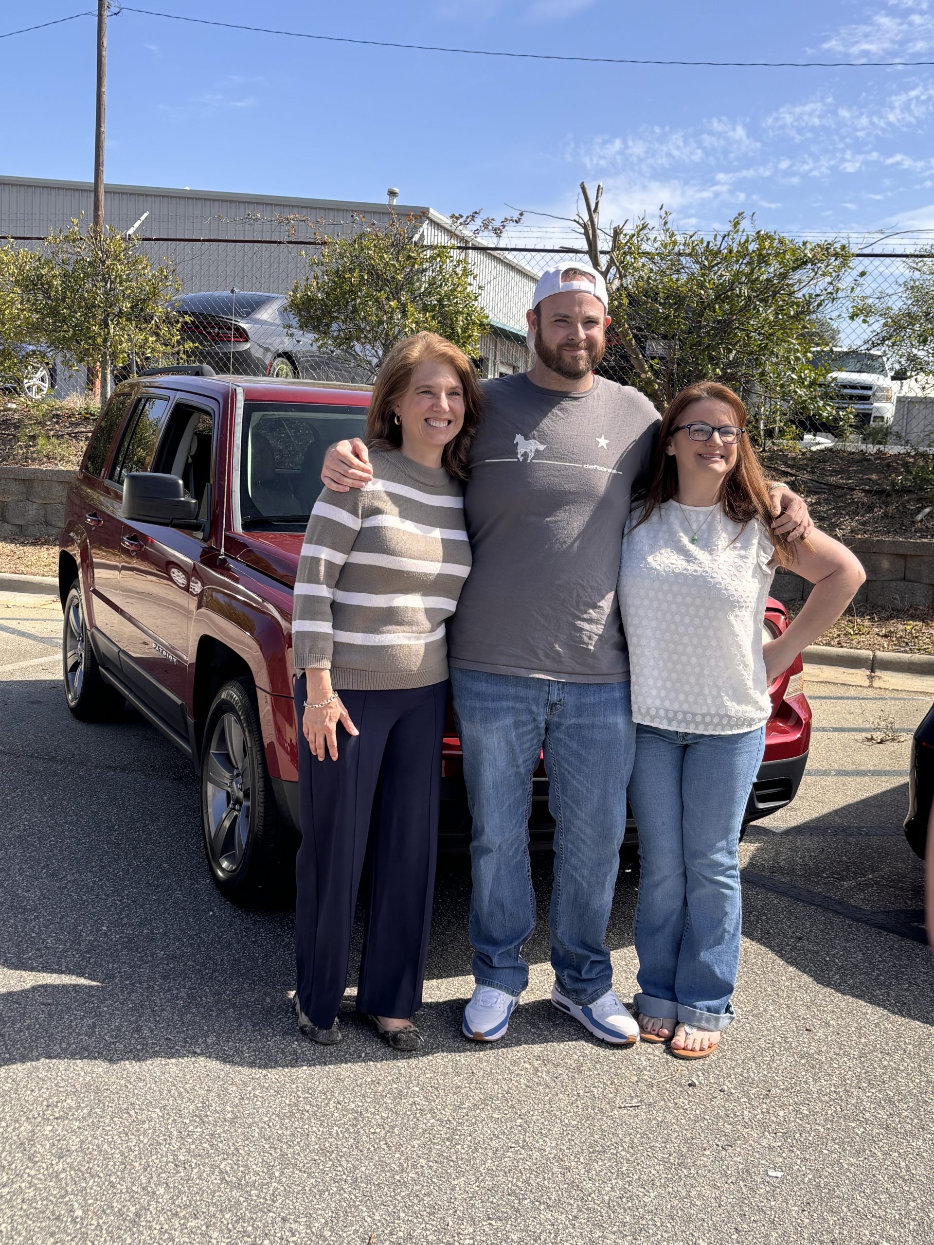 3 people standing in front of a car smiling.