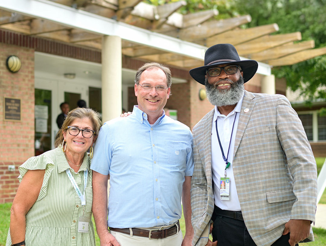 Three adults smiling outside a building with columns and pergola
