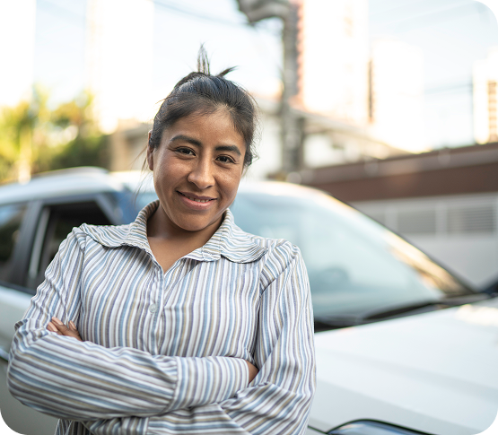 Person smiling confidently standing with arms crossed near a white car