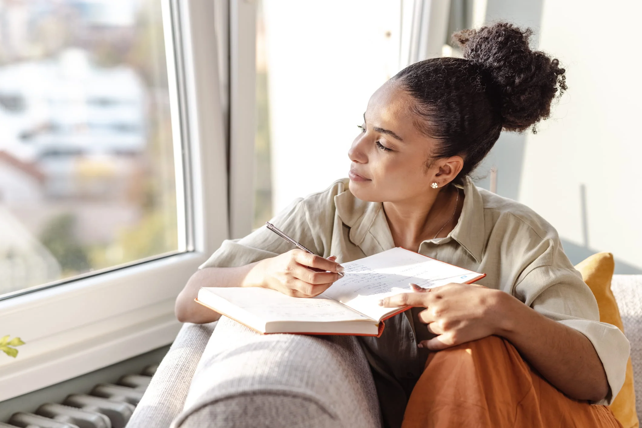 Woman sitting by window writing in notebook with pen