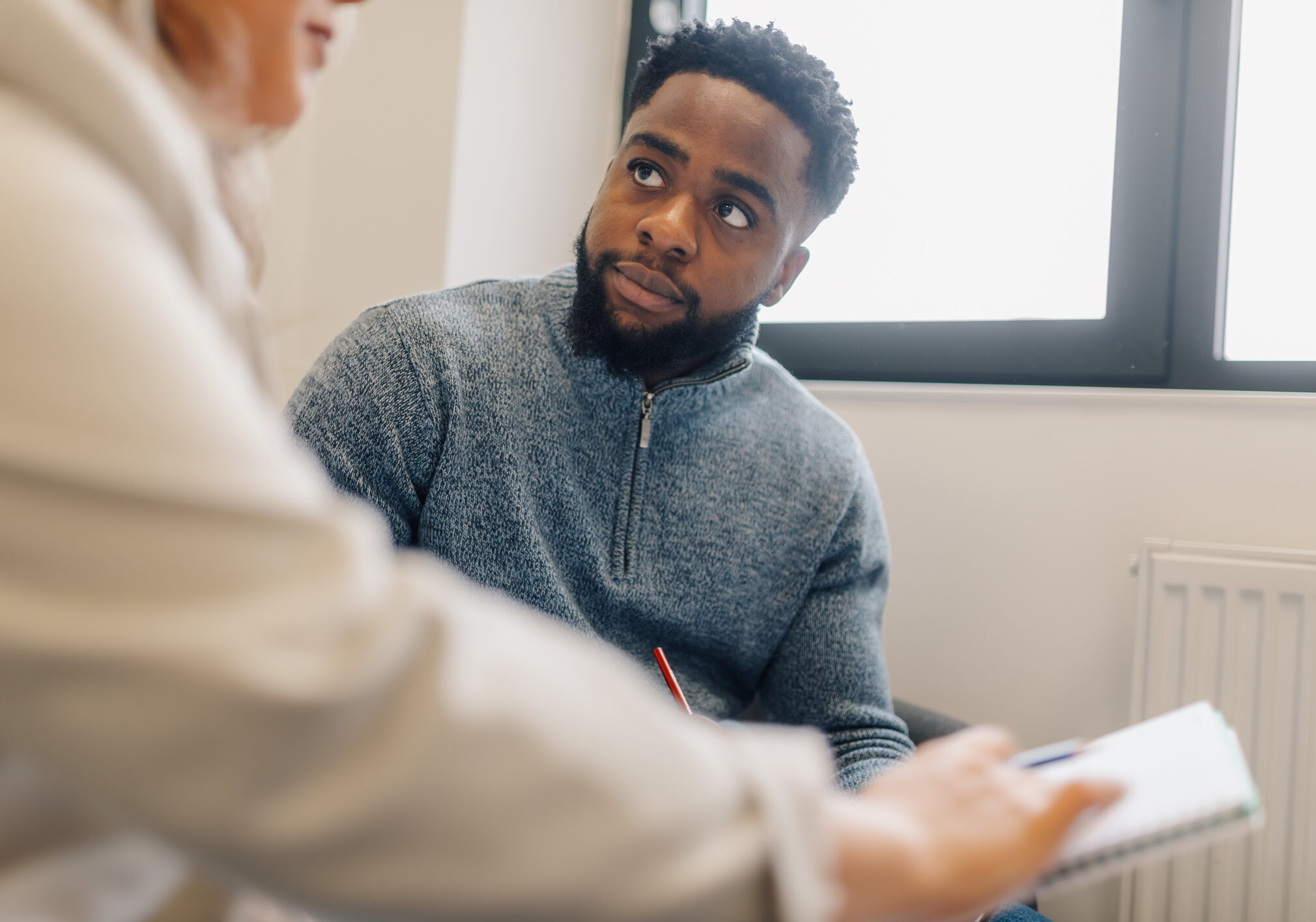 Man attentively listening to counselor taking notes during therapy session
