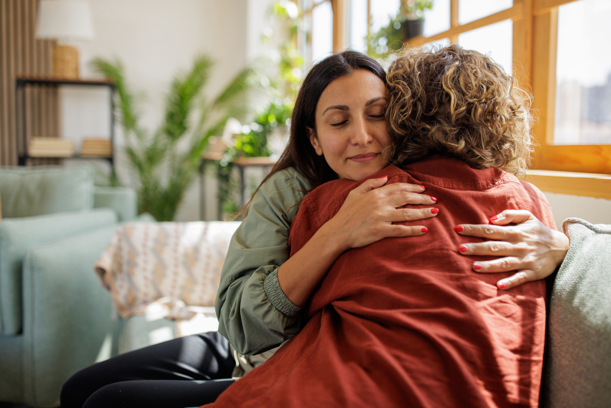 Two women hugging in a sunlit living room