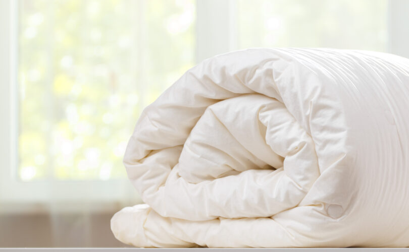 Rolled white duvet placed on a light-colored surface near a window