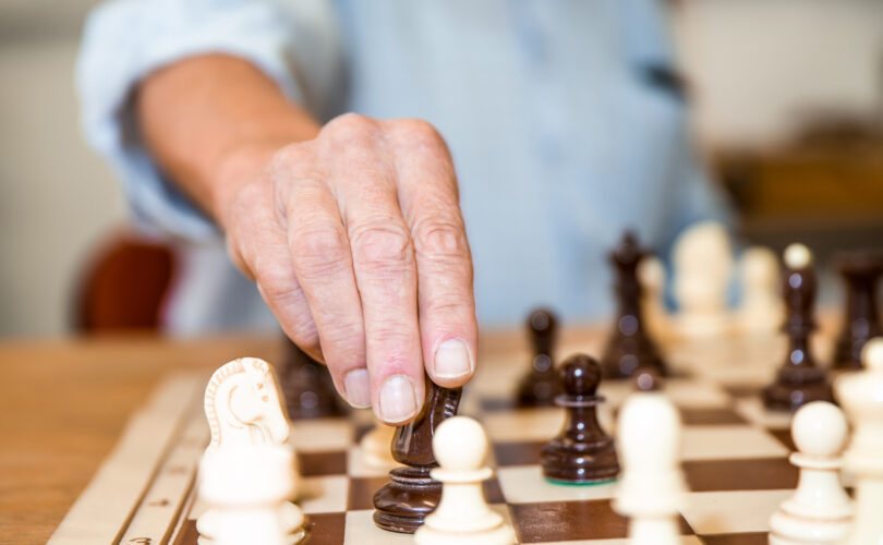 Hand moving a black knight chess piece on chessboard
