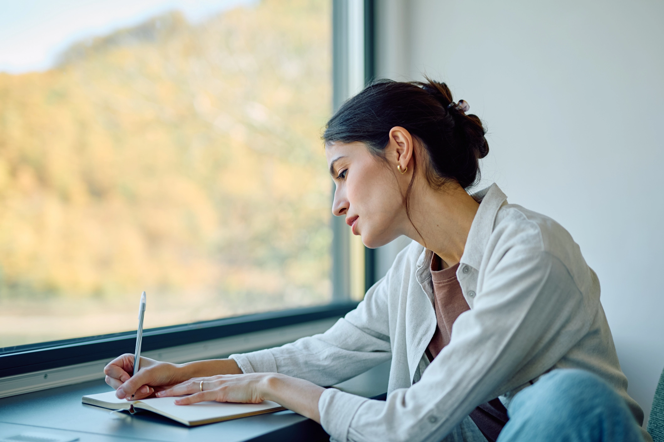 Woman, sitting next to a window, writing in a journal