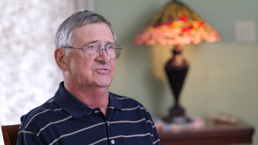 Elderly man with glasses wearing navy striped polo shirt indoors