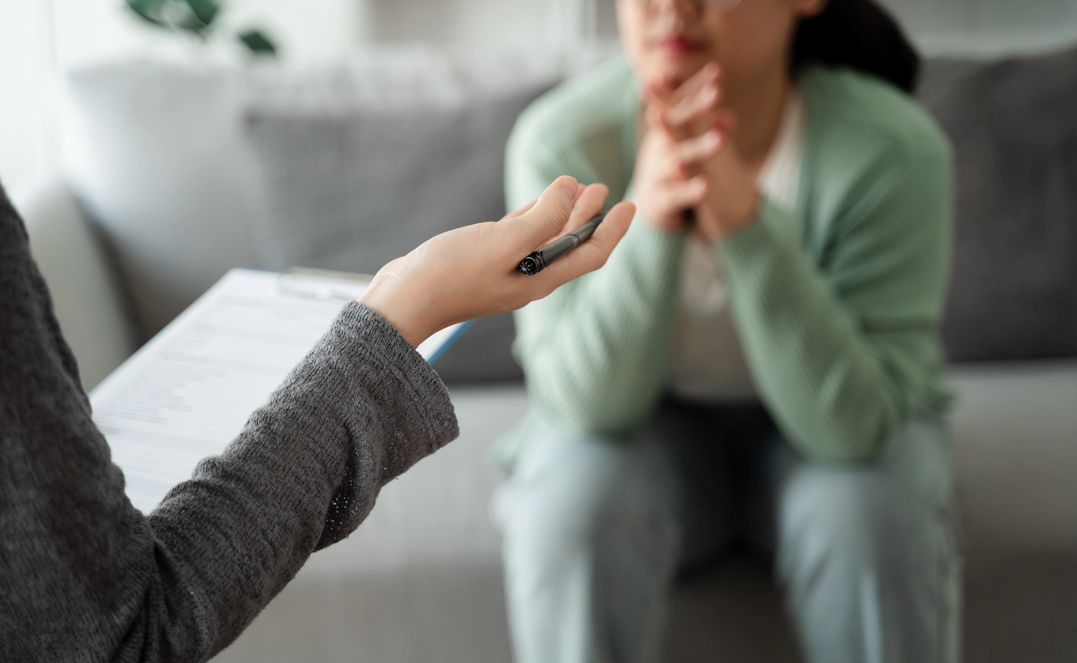 Woman sitting on couch with hands folded , looking at therapist with hands open like she is explaining something