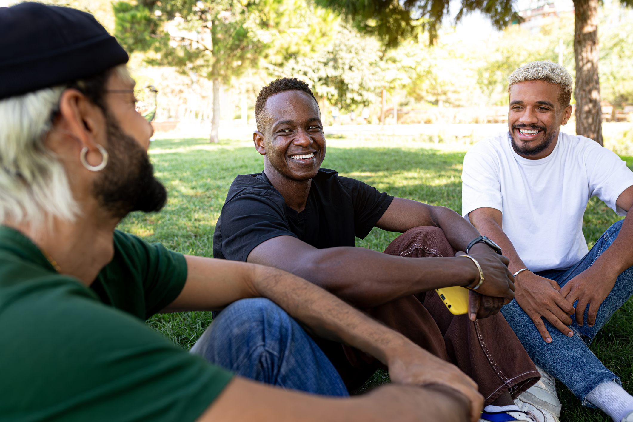 Three young men sitting on grass, laughing and enjoying each other's company