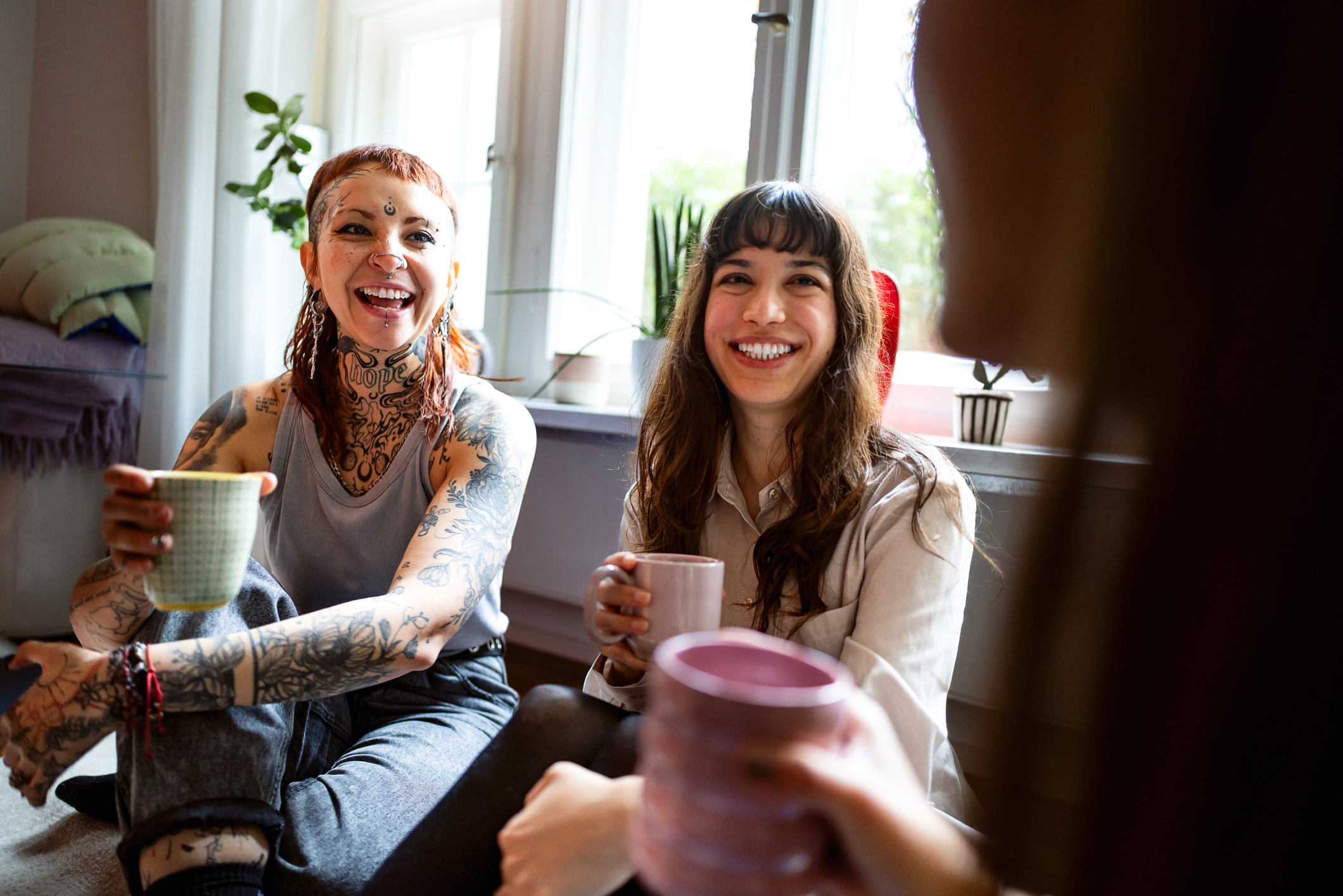 Three women sitting on floor, smiling and holding coffee mugs