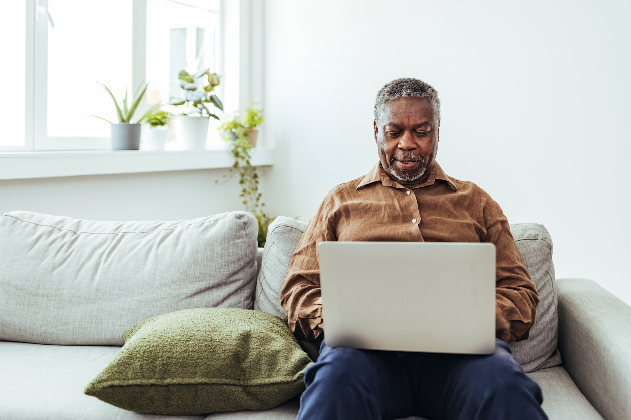 Man sitting on couch working on laptop with plants in background