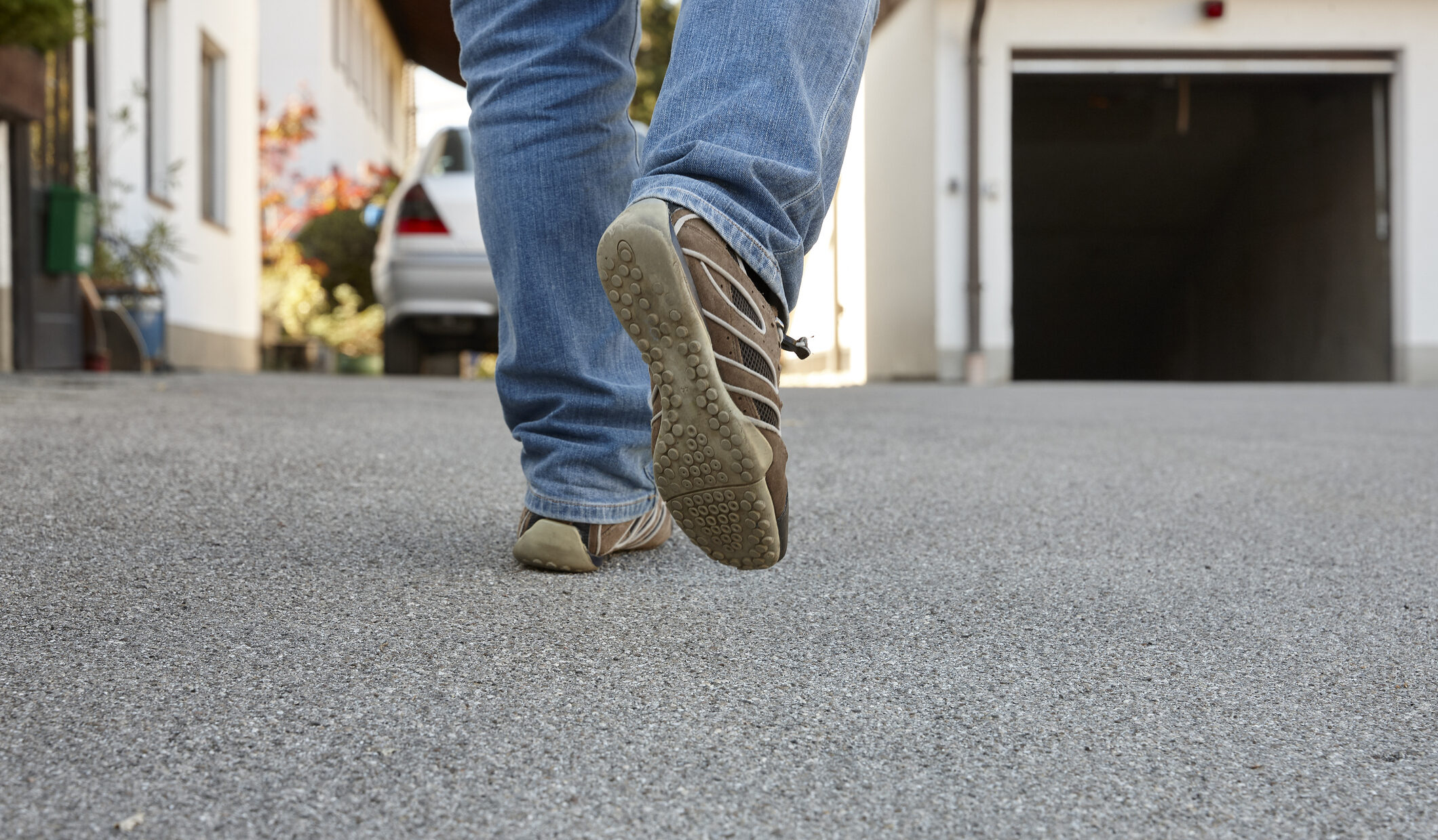 Person walking on paved residential street in blue jeans and brown shoes