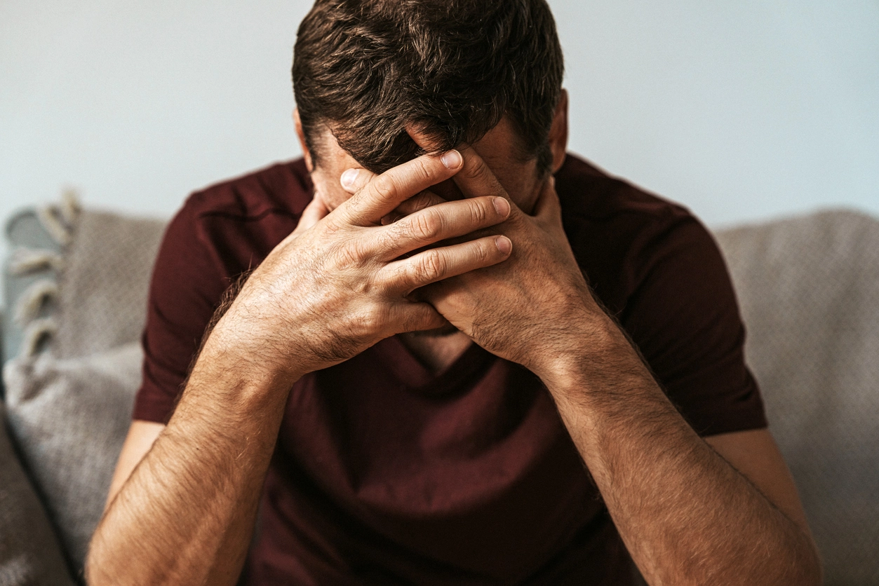 Man with head in hands. he is sitting on a couch with his hands covering his face.