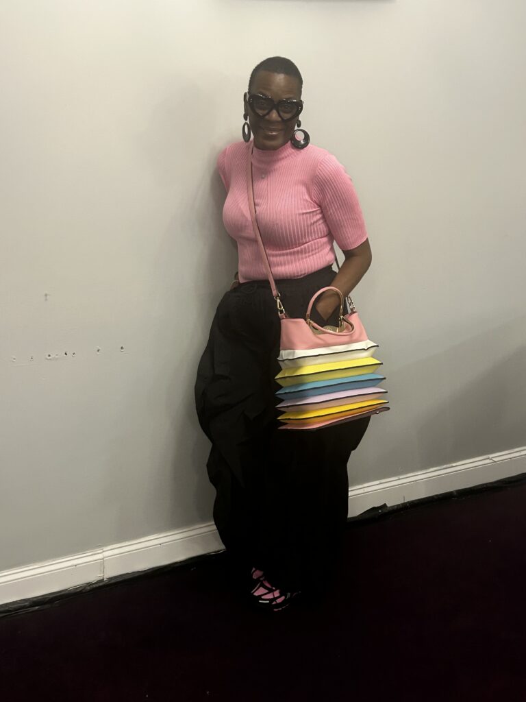 black woman wearing pink shirt smiling and leaning against wall